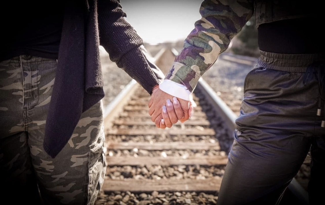 Two people locking hands on a train track — a picture of partnership