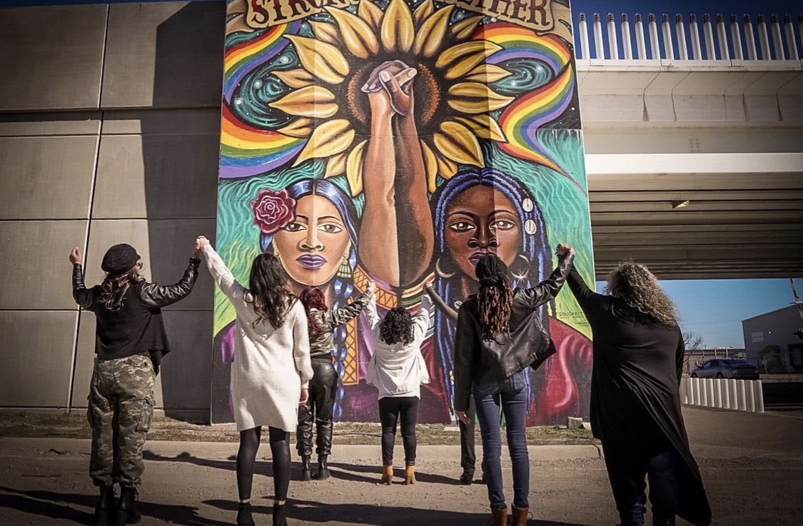 Women joining hands in front of a Wichita sisterhood mural
